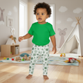 Child wearing a green shirt and patterned pants in a playroom.