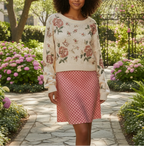 Woman wearing a floral sweater and pink checkered skirt in a garden setting