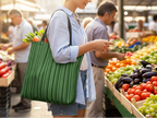 Person shopping at a farmers market with a green striped bag filled with groceries.