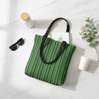 Green striped tote bag with black handle on a white surface with sunglasses and flowers.
