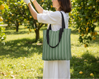Person holding a green striped tote bag in an orchard