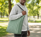 Man holding a green and white striped bag in a park