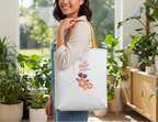Woman holding a tote bag with floral design and text in a home setting with plants.