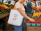 Person shopping at a farmers market with a tote bag that says 'Grow Girl!'.