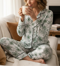 Woman in green floral pajamas holding a mug in a cozy living room.