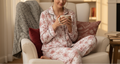 Woman in floral pajamas sitting on a couch in a cozy living room, using a smartphone.
