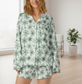 Woman wearing a green floral pajama set in a room with a plant and chair.