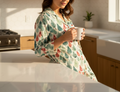Woman in a floral robe holding a mug in a kitchen.