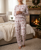 Woman in floral pajamas holding a mug in a cozy living room with a fireplace and Christmas decorations.