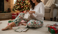 Woman in festive pajama pants sitting on the floor with Christmas presents in a decorated living room.