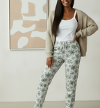 Woman wearing a white tank top and floral pants with a beige cardigan, standing against a neutral background.