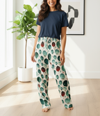 Woman wearing a navy top and patterned pants in a bright room with a plant and abstract art.