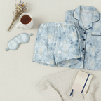 Floral pajama set with eye mask, mug, and notebook on a light surface