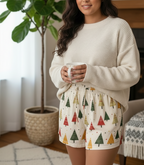 Woman wearing a white sweater and patterned shorts holding a mug indoors.