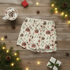 Christmas-themed pajama shorts on a wooden surface with a cup of hot chocolate, lights, and pine cones.