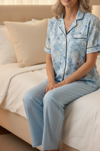 Woman wearing a light blue floral pajama set sitting on a bed.