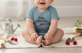Baby wearing a 'Baby Gardener' onesie with gardening tools and plants on a light background