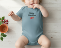 Baby in a 'Baby Gardener' onesie on a wooden floor with plants.