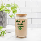 Glass jar with a wooden lid labeled 'Wake Up & Garden' on a white surface with a plant in the background.
