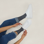 Person wearing white sneakers and blue jeans, sitting on a light-colored floor.