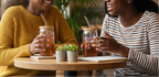 Two people sitting at a table with drinks and plants, smiling.