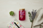 Jar with 'Grow, Girl!' text on a light surface with a plant, notebook, and pen.