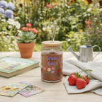 Mason jar with 'Grow, Girl!' text and floral designs on a table with strawberries and a garden background.