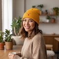 Woman wearing a yellow beanie and holding a mug in a cozy indoor setting with plants.