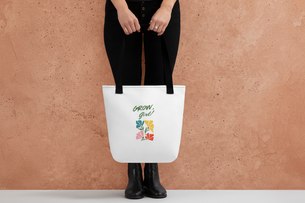 White tote bag with 'Grow Girl!' text and floral design held by a person against a gray background