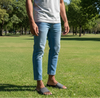 Man wearing a light gray t-shirt and blue jeans standing on grass with trees in the background