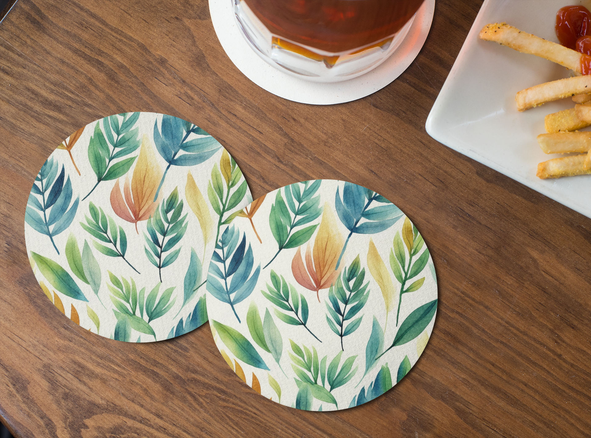 Two leaf-patterned coasters on a wooden table with a glass of tea and a plate of food.