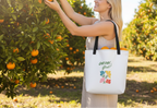 Woman in an orchard holding a tote bag with 'Grow Girl!' text and floral design.
