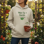 Person wearing a hoodie with 'Wake Up & Garden' text holding a potted plant in a garden setting