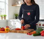 Woman in a kitchen wearing a navy blue sweatshirt with 'Gardening Rocks' text and a peach graphic, cutting vegetables.