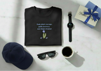 Black t-shirt with text, sunglasses, coffee cup, watch, and cap on a white surface.