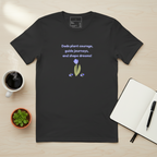 Black t-shirt with a motivational quote and floral design on a wooden surface with a cup of coffee, plant, and notebook.