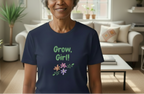 Person wearing a navy blue t-shirt with 'Grow, Girl!' text and floral designs in a living room.