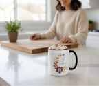 Mug with floral design and whipped cream on a kitchen counter with a person in the background.