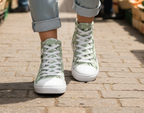 Green floral high-top sneakers with white soles worn on a paved surface.