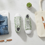 Green sneakers with white laces on a light gray surface, surrounded by a tote bag, denim jacket, and watches.